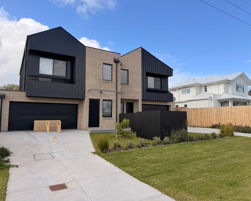 A completed pair of two-storey townhouses with dark cladding and brick, from Michael's residential development work (house numbers blurred)