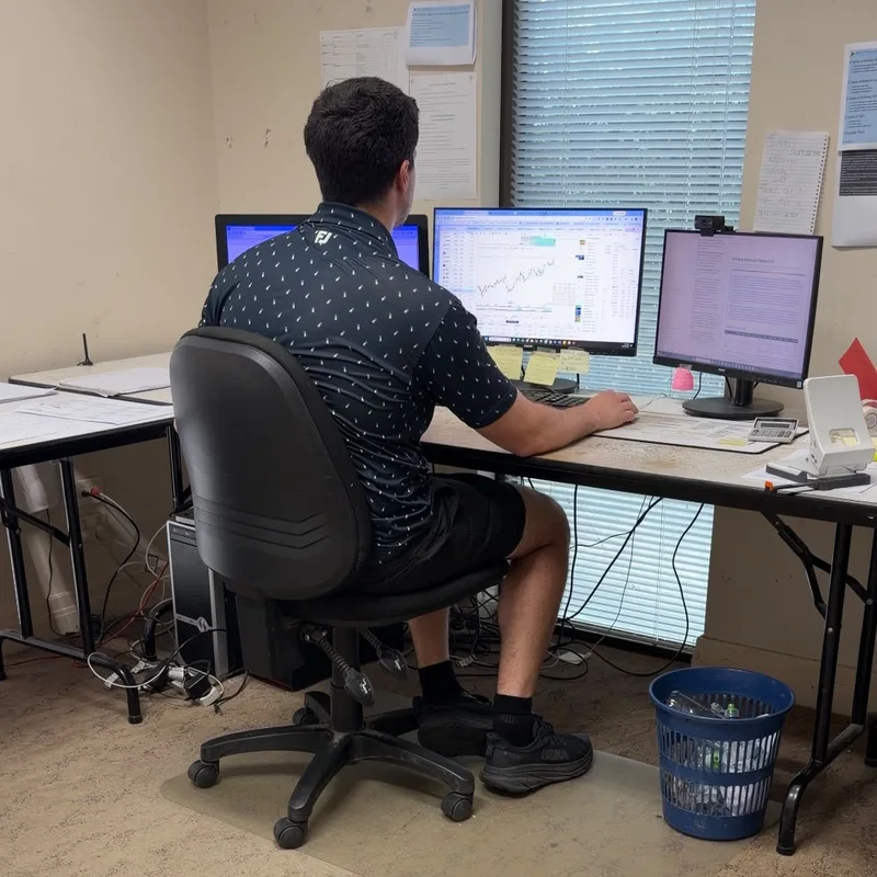 Michael at his trading desk with three monitors showing charts, research and a portfolio dashboard